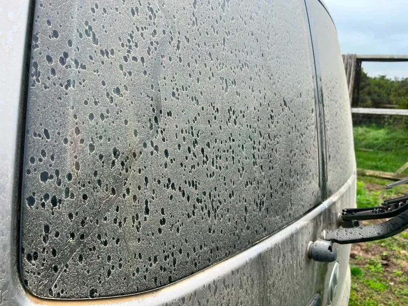 Close-up of a dirty, spotted vehicle window before washing